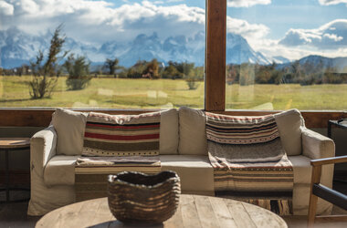 Sofa mit gemusterten Decken vor Panoramafenster mit Blick auf das Paine-Massiv in Patagonien, Chile.