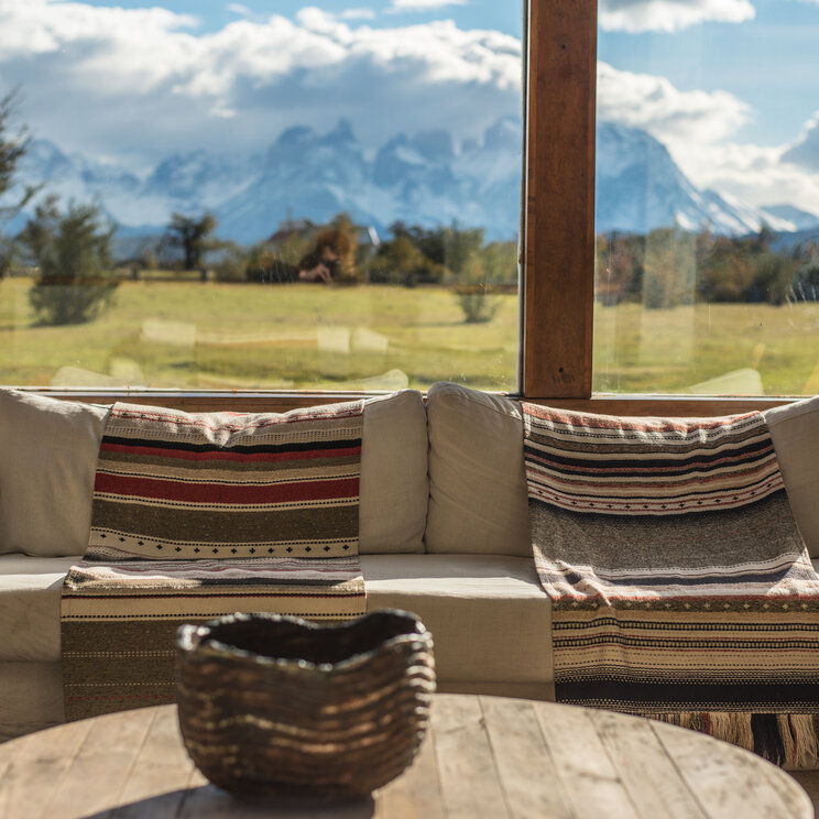 Sofa mit gemusterten Decken vor Panoramafenster mit Blick auf das Paine-Massiv in Patagonien, Chile.