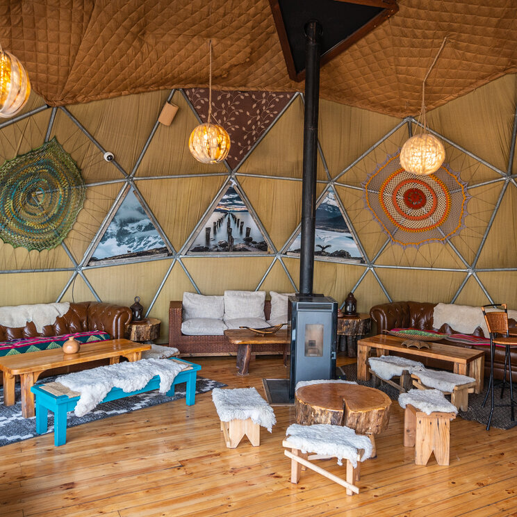 Loungebereich im Bar Dome mit Ledersofas, Holztischen und traditioneller Dekoration im EcoCamp Patagonia, Chile.
