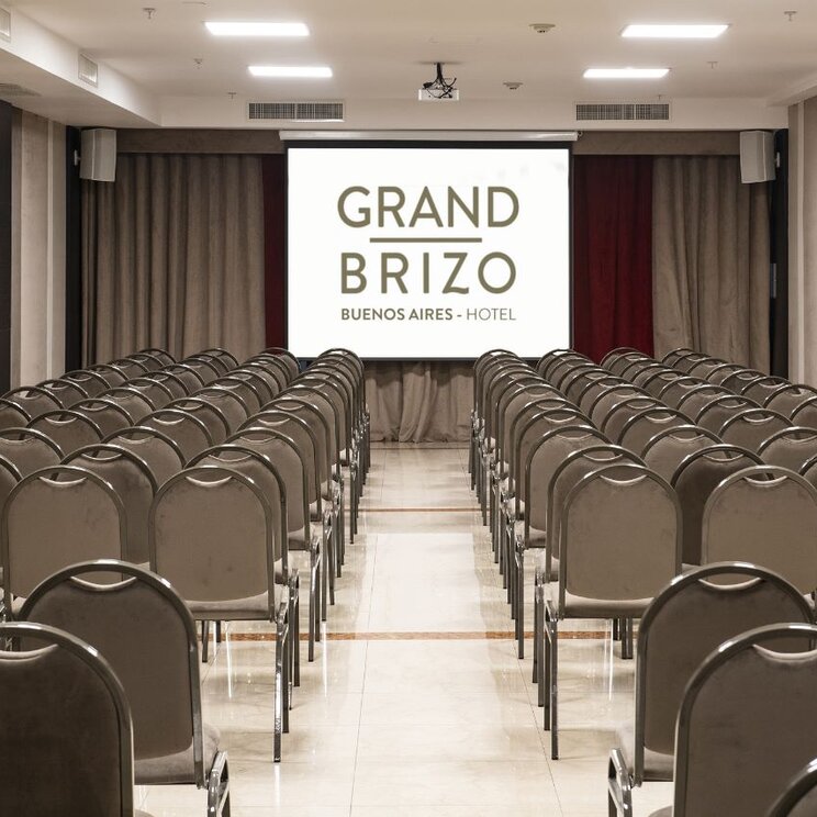 Konferenzraum mit Stuhlreihen und einer Leinwand mit Logo im Grand Brizo Hotel in Buenos Aires.