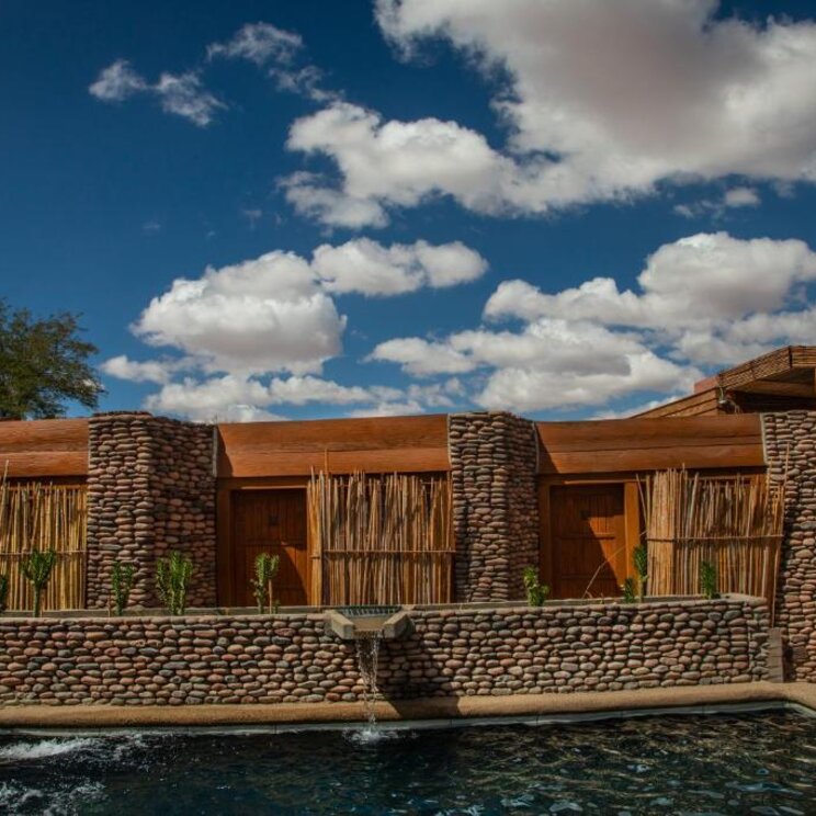 Aussenpool vor Gebaeudefassade mit Natursteinmauern, Holztueren und Schilfmatten in der Atacama Wueste, Chile.