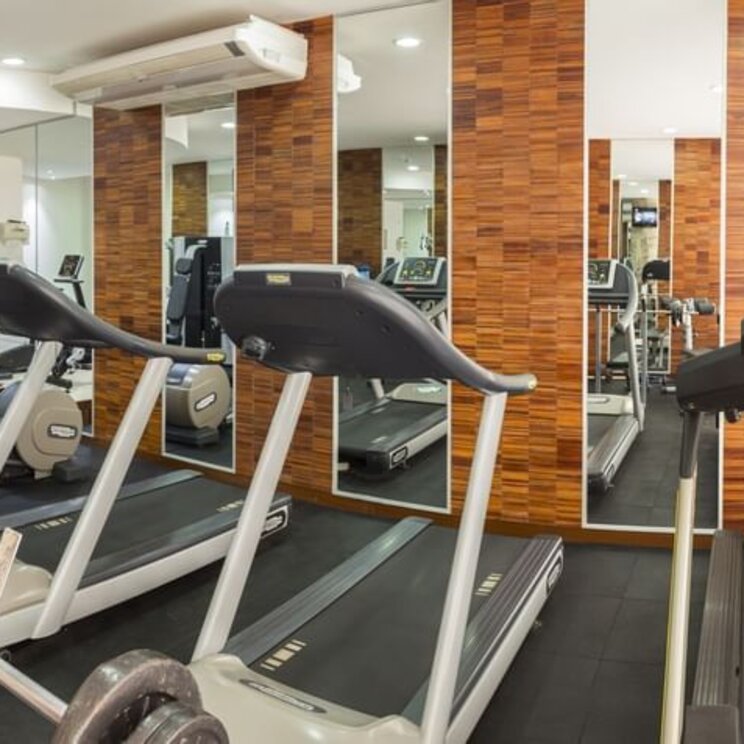 Fitnessraum im Camino Real Hotel Santa Cruz mit Laufbaendern vor holzverkleideten Waenden und Spiegeln.