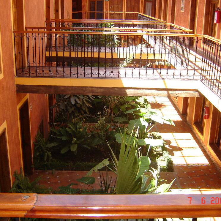 Innenhof eines Hotels in Palenque mit Holzbalkonen, Geländern und tropischer Bepflanzung.