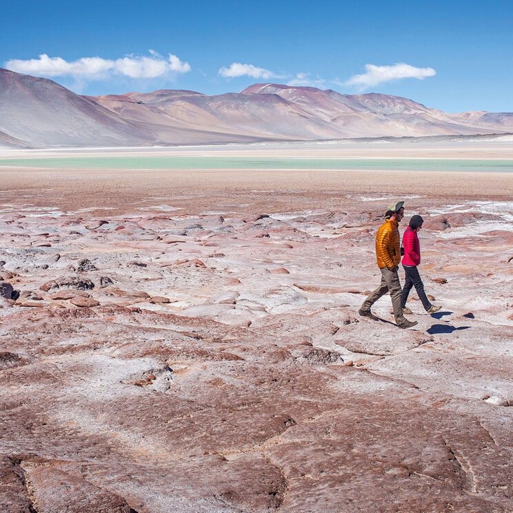Piedras Rojas im Atacama Hochland mit rötlichen Felsformationen, Salzflächen und Lagunen vor vulkanischer Andenkulisse.