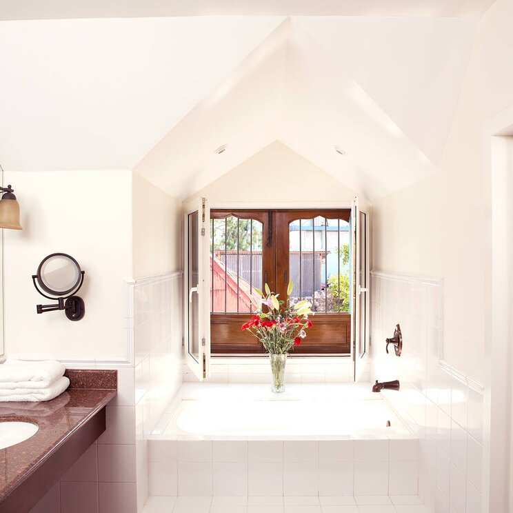 Badezimmer mit Marmorwaschtisch, weissen Fliesen und Badewanne unter einem Fenster im Hotel Isla de Flores.
