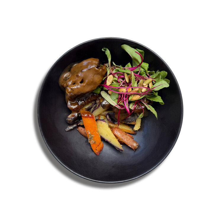 Gourmetteller in der Casa Gastón bei Uyuni mit geschmortem Fleisch in Sauce, Ofengemüse und frischem Blattsalat auf schwarzem Teller.