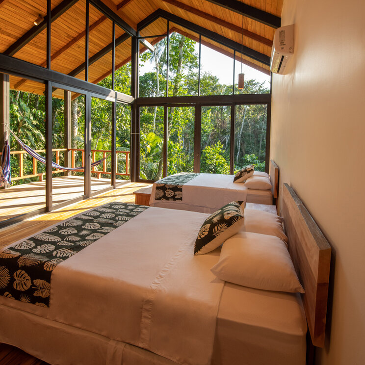 Helles Doppelzimmer mit Glasfront, Holzboden und Blick in den Regenwald der Sacha Lodge, Ecuador.