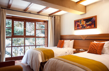 Hotelzimmer mit zwei Einzelbetten, gelben Tagesdecken, Wandbild und Fenster zur bewachsenen Felswand.