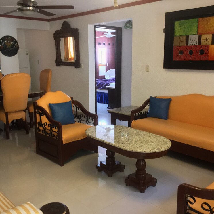 Wohnbereich einer Suite im Hotel Las Golondrinas in Playa del Carmen mit Sofa, Sesseln, Esstisch und Zugang zum Schlafzimmer.