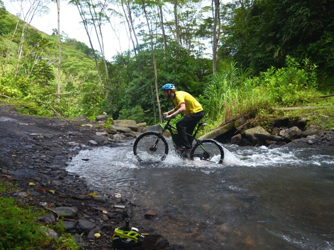 Ein Mountainbiker fährt in Otanche durch einen kleinen Fluss mitten im grünen Dschungel.