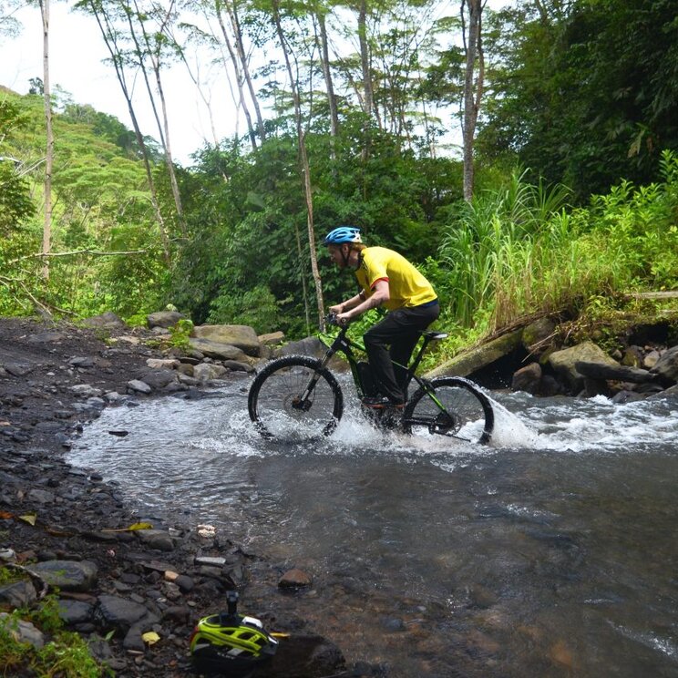 Ein Mountainbiker fährt in Otanche durch einen kleinen Fluss mitten im grünen Dschungel.