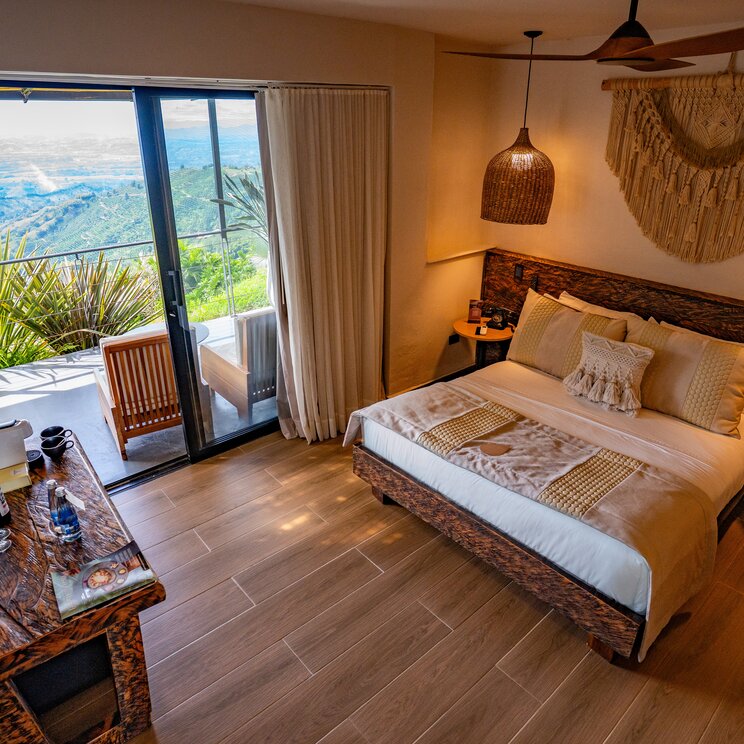 Hotelzimmer mit Holzboden, Doppelbett und geoeffneter Balkontuer zur Berglandschaft.