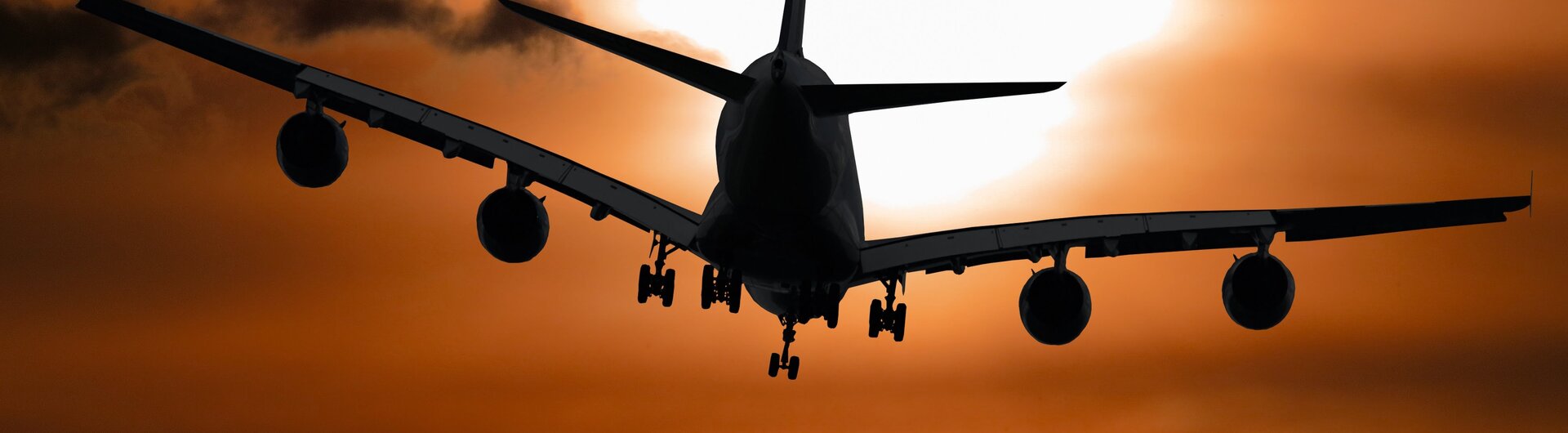 Silhouette eines vierstrahligen Passagierflugzeugs im Anflug vor dem glühenden Kreis der untergehenden Sonne