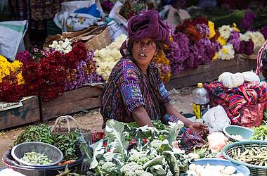 Marktverkäuferin in tradionell farbenfroher Kleidung mit Gemüse vor sich