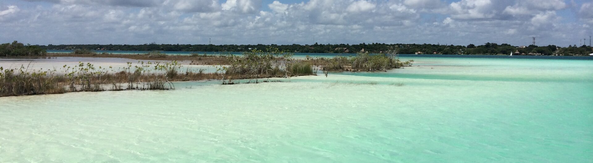 Ein hölzerner Badesteg mit einer Palapa-Hütte führt in das türkisfarbene Wasser von Bacalar Mexiko.