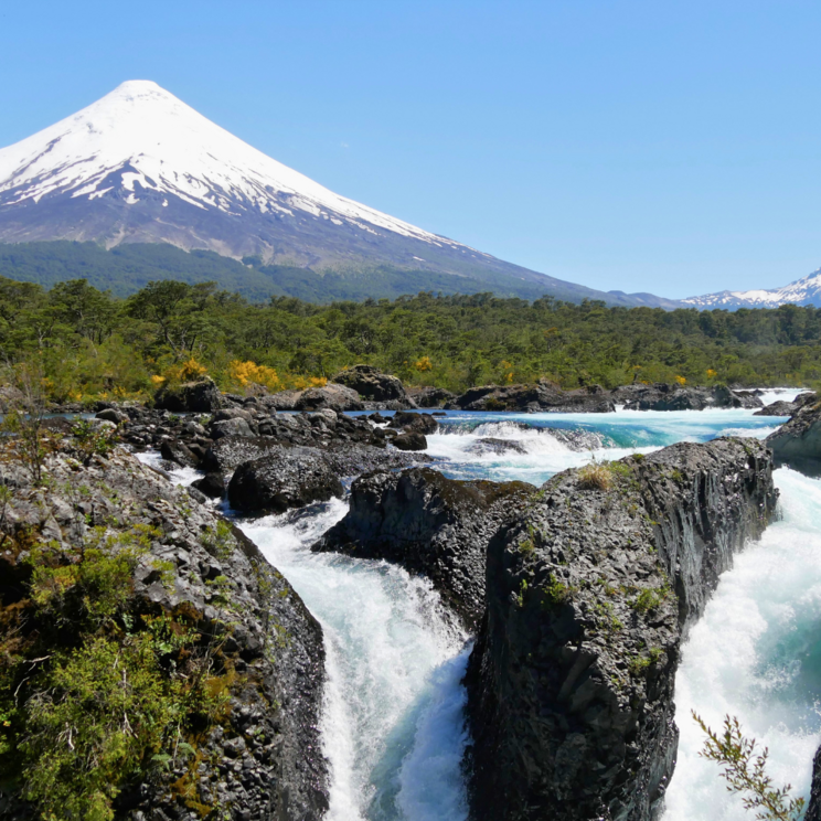Saltos de Petrohué mit tosenden Wasserfällen aus Lavagestein und Blick auf den schneebedeckten Vulkan Osorno im chilenischen Seengebiet.
