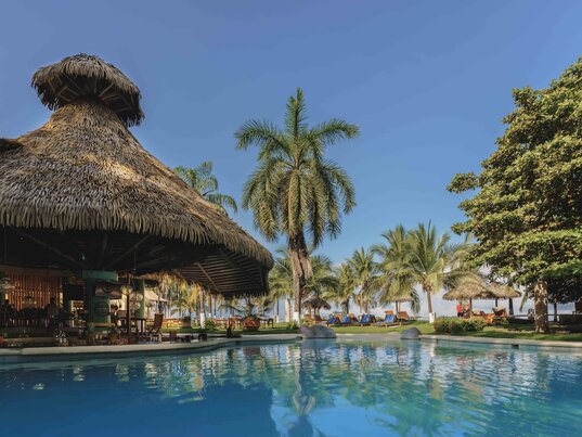 Poolbar mit Strohdach direkt am Swimmingpool im tropischen Garten der Hotelanlage