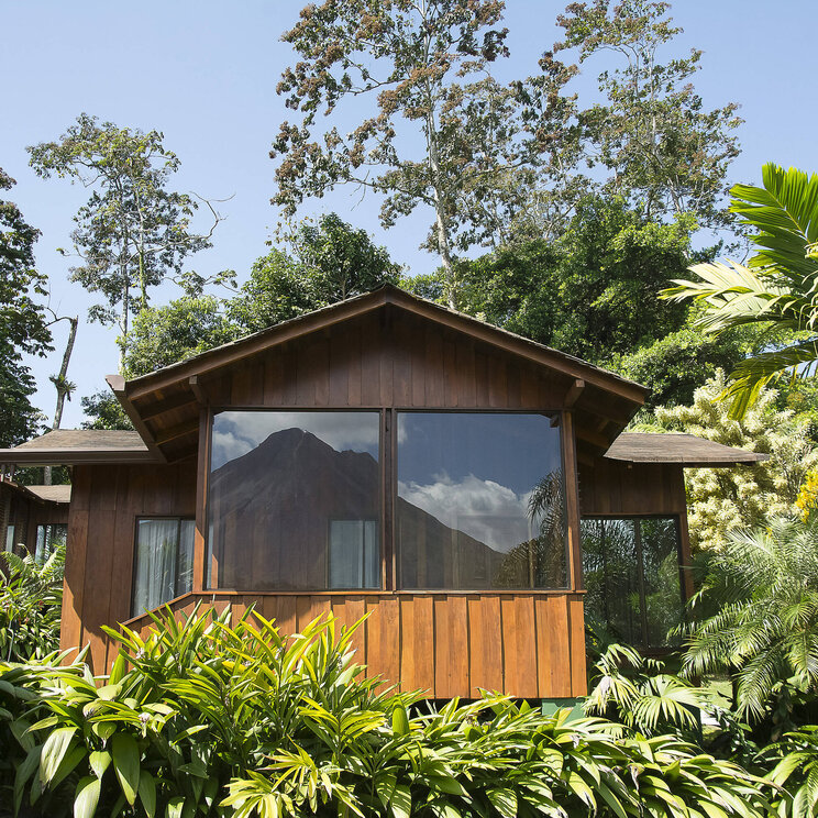 Superior-Bungalow im Hotel Arenal Paraíso Resort & Spa in La Fortuna, Costa Rica, mit großer Fensterfront und Blick auf den Vulkan Arenal, umgeben von tropischer Vegetation.