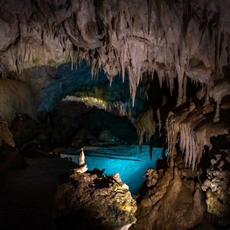 Beleuchtete Tropfsteinhöhle mit unterirdischem Wasserbecken in Belize.