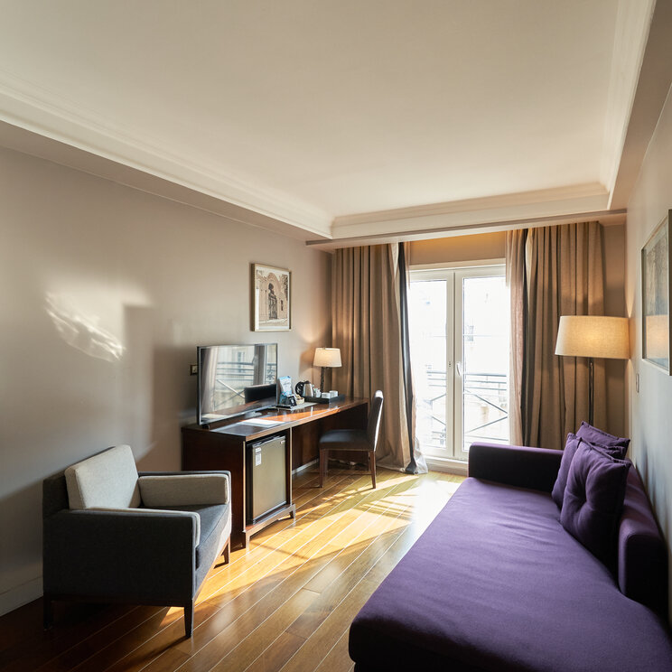 Wohnbereich der Suite im Carles Hotel in Buenos Aires mit lila Sofa, Sessel, Schreibtisch, Fernseher und Balkontür.