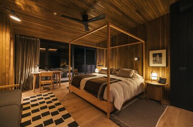 Schlafzimmer im Tierra Atacama Chile mit Holzwänden, Himmelbett, Ventilator und warmer Beleuchtung bei Nacht.