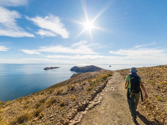 Ein Wanderer mit Rucksack läuft auf einem Pfad der Isla del Sol in Bolivien mit Blick auf den Titicacasee.