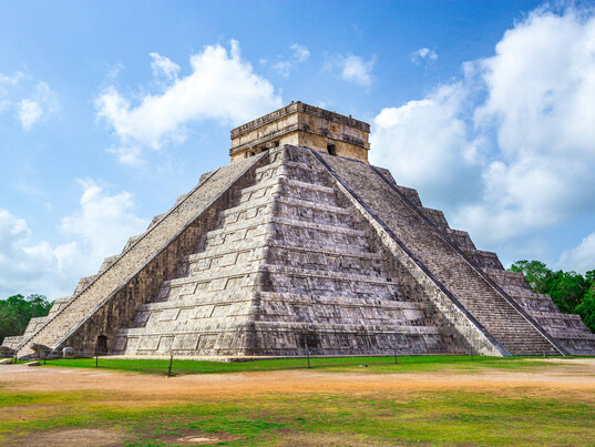 Die Pyramide El Castillo in Chichén Itzá, Mexiko, ein ikonisches Maya-Bauwerk umgeben von grüner Landschaft.