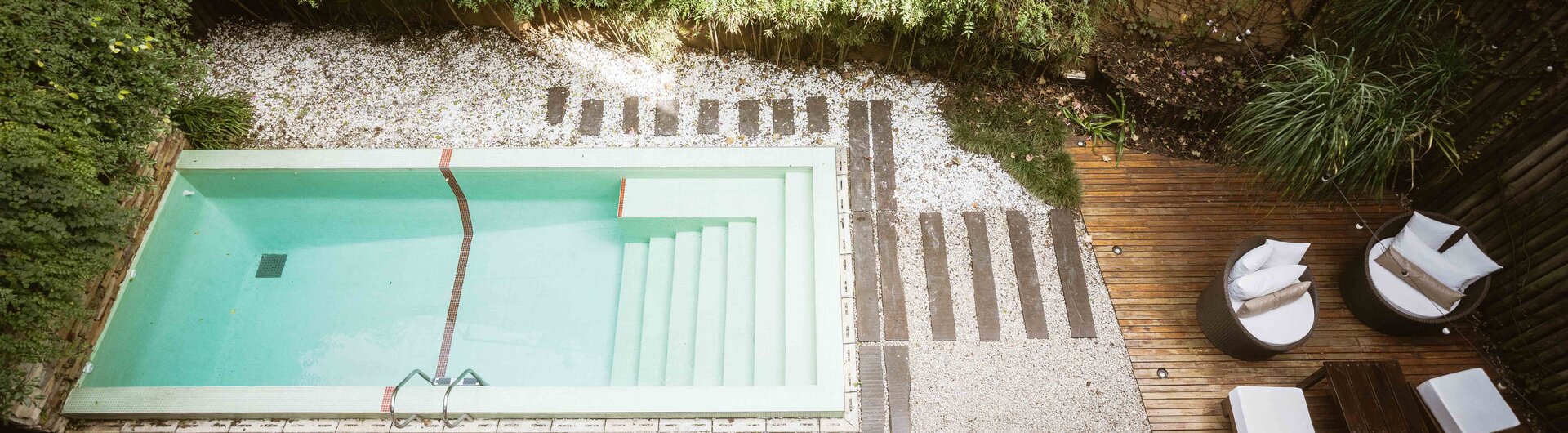 Pool mit Liegen und Holzdeck in einem gruenen Hotelinnenhof in Buenos Aires.