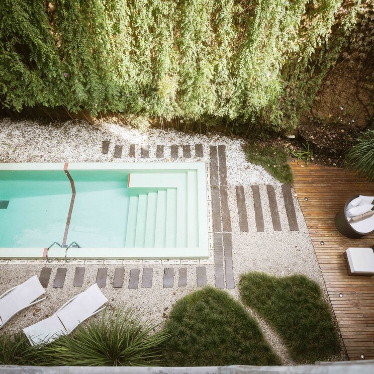 Pool mit Liegen und Holzdeck in einem gruenen Hotelinnenhof in Buenos Aires.