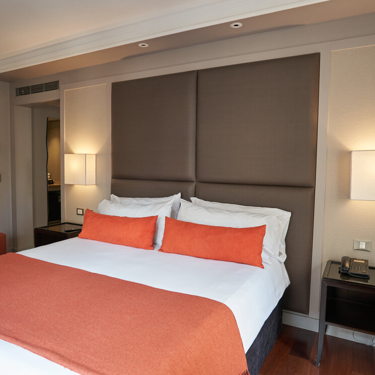 Superior-Doppelzimmer im Carles Hotel in Buenos Aires mit großem Kopfteil, orangefarbenen Kissen und Nachttischen.