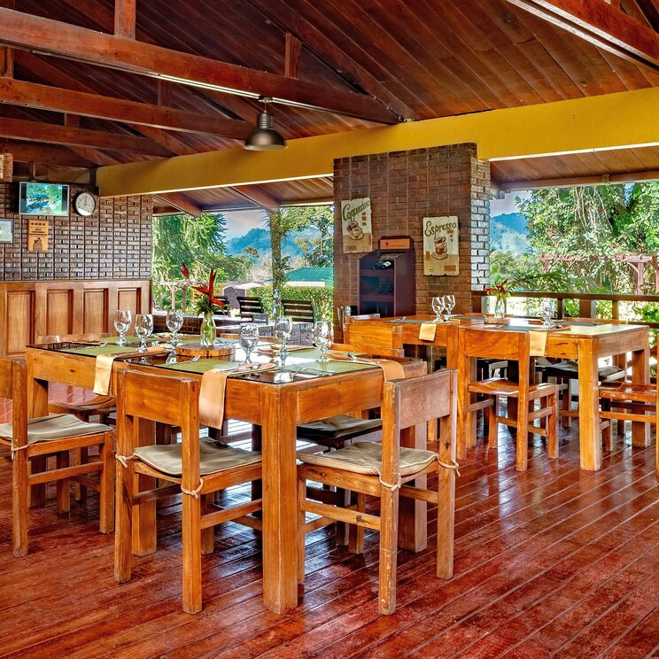 Offenes Restaurant im Hotel Villa Florencia in Costa Rica mit Holzmöbeln, gedeckten Tischen und Blick ins Grüne.