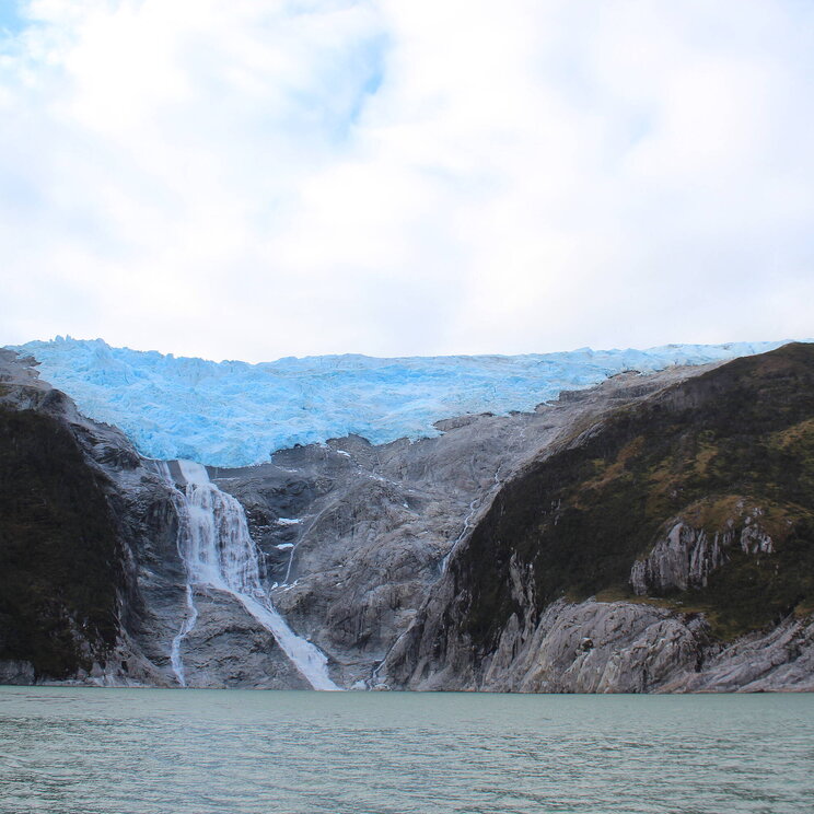 Gletscher mit Wasserfall, der in eine Bucht auf der Isla Navarino in Patagonien, Chile, mündet.