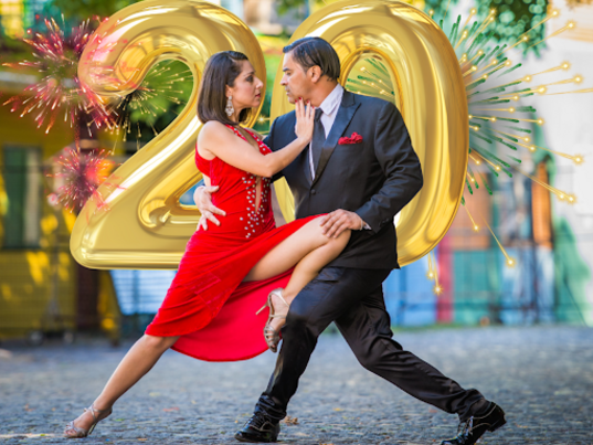 Tanzendes Paar in elegantem roten Kleid und Anzug beim Tango vor goldenen Jubiläumsballons mit der Zahl 20, Symbol für Gateways Jubiläums-Highlights.
